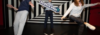 Three younger people standing in an illusions room holding a science week sign.