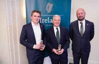 Three men dressed in suits while two of the men are holding trophies