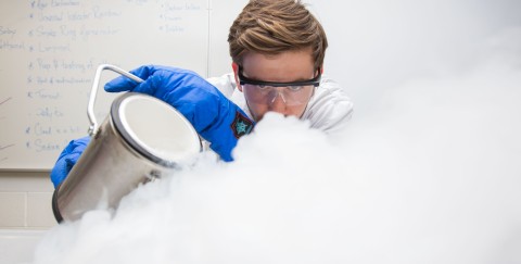 A Scientist wearing blue Ice gloves is pouring dry ice onto a table
