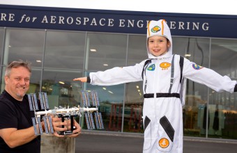 A Child pictured at Aerospace Studies dressed as a astronaut with a older man standing holding a crafted space object.