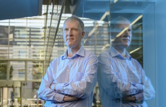 Brian Corbett from Tyndall National Institute standing up against a glass wall mirroring his reflect.