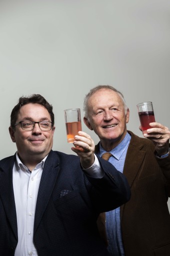 Two men dressed professionally holding up glasses with a drink in them