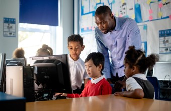 A teacher standing over students as they use the classroom computer