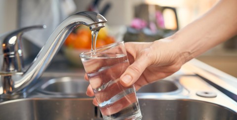 person filling a glass with water from a tap at home